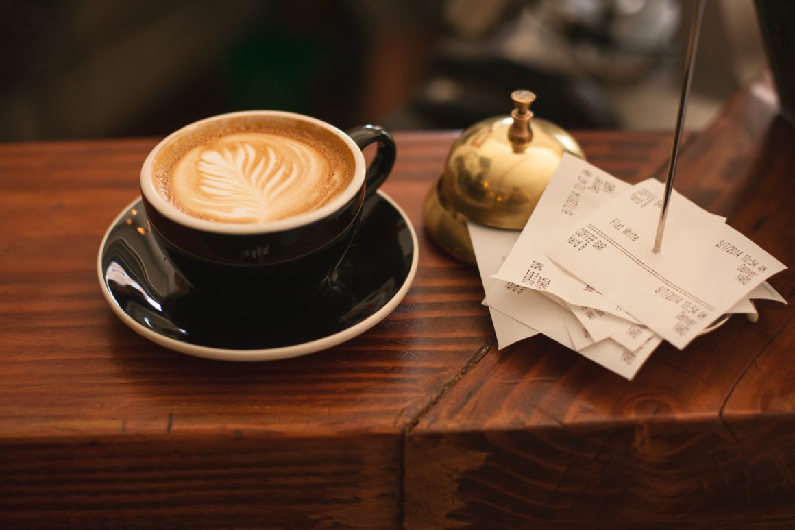 Coffee cup with latte art beside stacked paper receipts on wooden counter