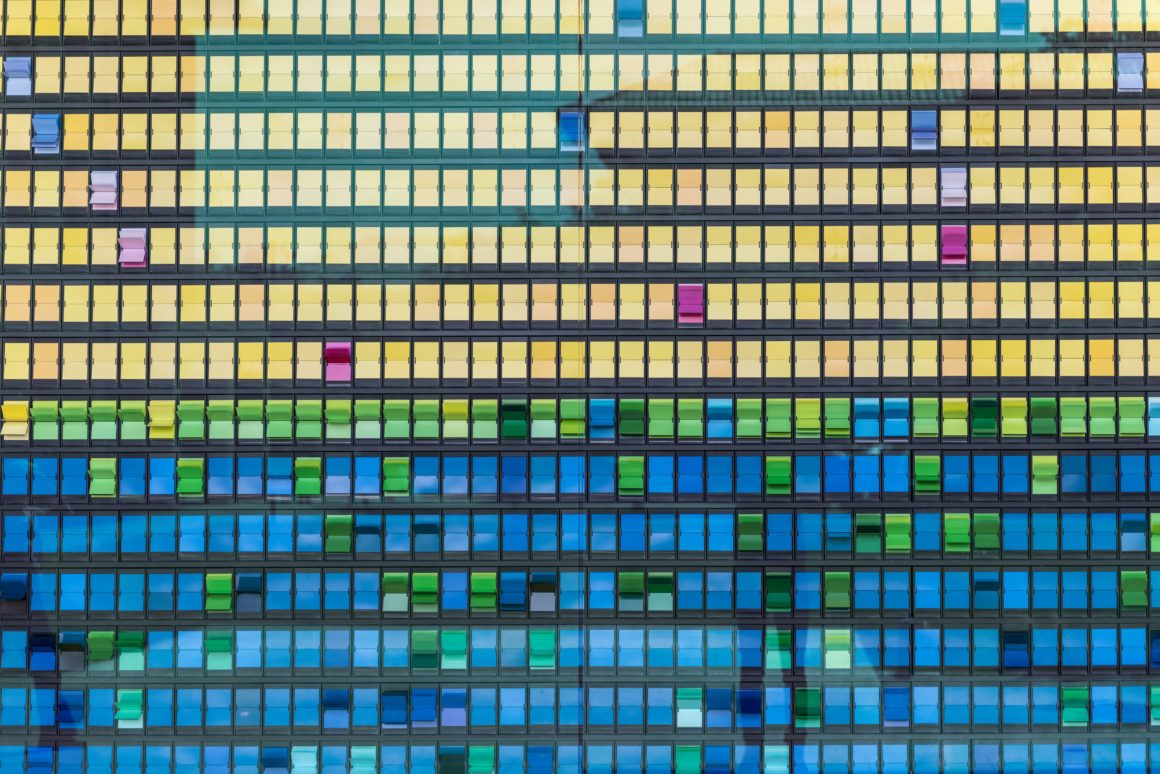 Close-up of colorful office building glass facade with rows of yellow, green and blue windows
