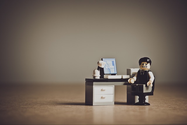 Lego figure sitting frustrated at a desk in front of a computer monitor