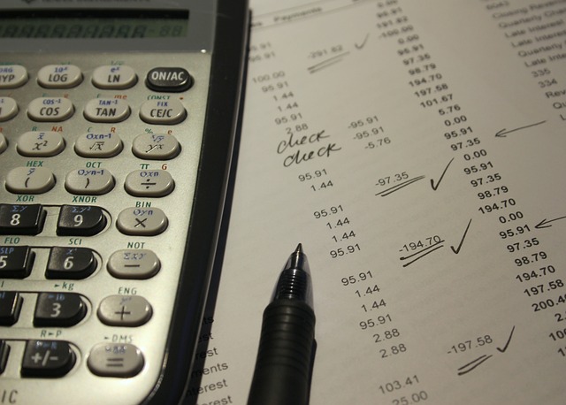 Calculator beside a printed financial ledger with checkmarks and handwritten notes