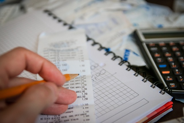 Hand holding a pencil over printed receipts and a notebook with a calculator nearby