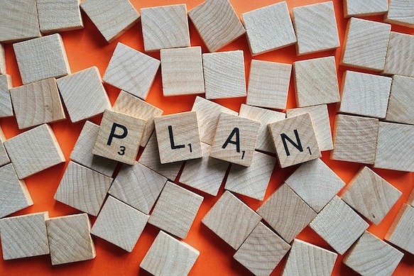 Wooden Scrabble letter tiles spelling PLAN scattered on an orange background