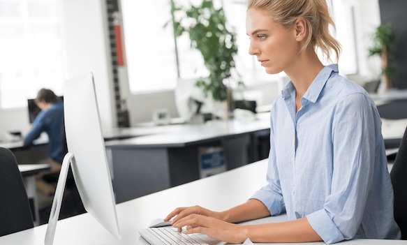 Woman typing at a desktop computer in a modern open-plan office
