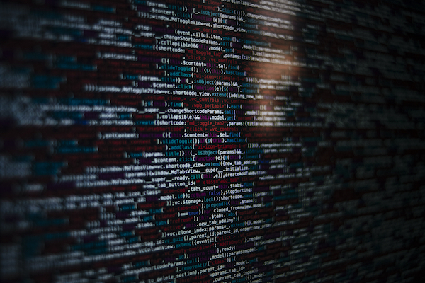 Closeup of a dark monitor displaying HTML and JavaScript source code with colorful syntax highlighting