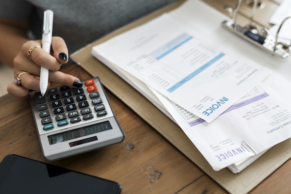 Woman using a calculator beside a stack of invoice documents on a desk