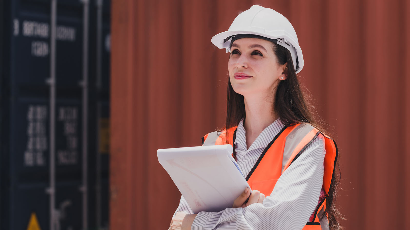 Logistics worker in hard hat and safety vest holding tablet at container yard